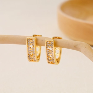 Detail shot of V-shaped gold earrings with floral zircon inlay on a wooden stand
