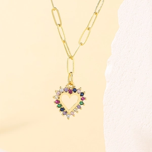 Gold paperclip necklace with multi-color gemstone heart pendant on a stone background