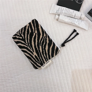 Detail of zebra-patterned knit pouch featuring a black tassel zipper and side logo tag