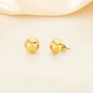 Detailed close-up of golden spherical stud earrings with high-polish metallic texture