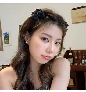 Elegant black satin bow hair clip with pearl earring detail on a female model