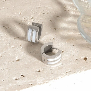 Detailed close-up of silver steel hoop earrings with white enamel inlay on stone surface