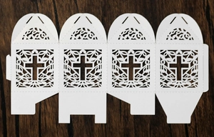 Flat lay of laser-cut white favor box with intricate cross and vine patterns on wood