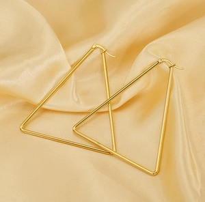 Macro shot of large golden geometric triangle hoop earrings on silk fabric background