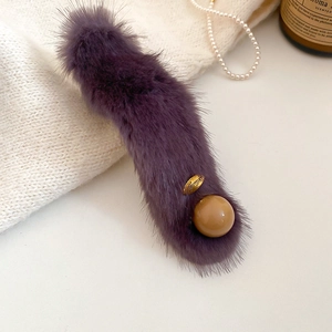 Close-up of purple plush hair clip with Lucky metal charm and resin pearl detail