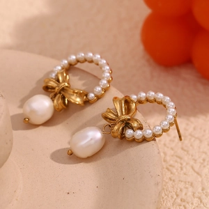 Detail of 18K gold-plated bow earrings with irregular pearl tassels on a warm background