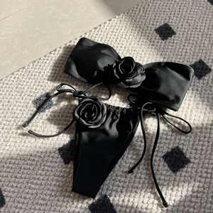 Black strapless bikini set with 3D rose details and side-tie bottoms on a plaid background
