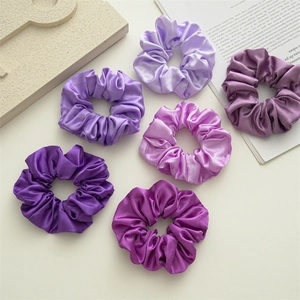 Flat lay of six satin scrunchies in various shades of purple on a white background