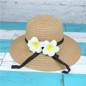 Detail of summer straw hat featuring Frangipani floral decor and black ribbon trim
