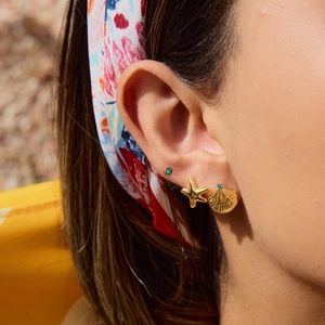 Close-up of gold starfish and shell stud earrings set with blue gemstones on a model