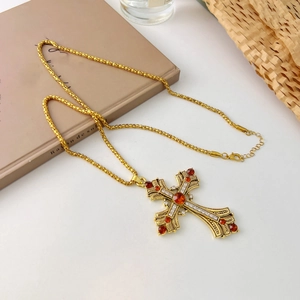 Vue détaillée d'un collier croix doré vintage avec cristaux rouges sur un bureau