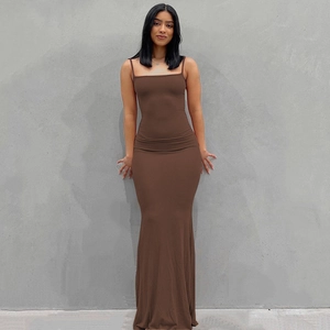 Vestido largo ajustado marrón con tirantes finos sobre un fondo arquitectónico minimalista