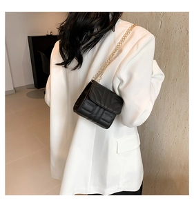 Detail of black quilted chain shoulder bag worn over a stylish white blazer for women