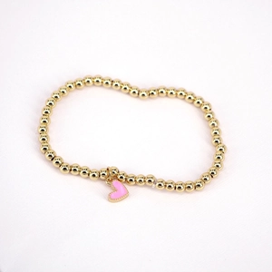 Detailed close-up of golden beaded bracelet featuring a pink enamel heart pendant charm