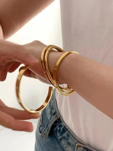 Detail of layered gold-plated titanium steel bracelets in smooth and textured styles