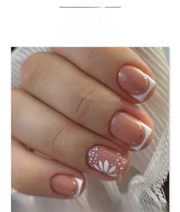 Detail of French white tip press-on nails with floral art and gold accents on lace