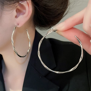 Detail view of silver twisted wave hoop earrings with polished irregular metallic texture