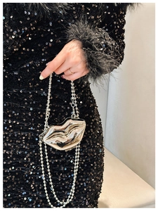 Detail of a golden lip-shaped metal evening bag featuring a silver bead chain strap