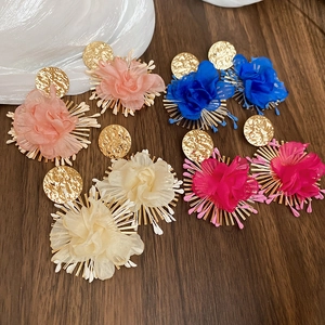 Detail view showing assorted colorful fabric flower pendant earrings on a wood background
