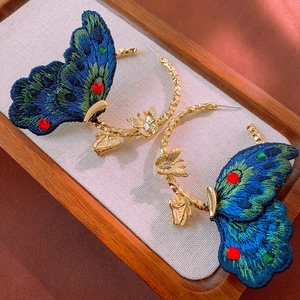 Detail of embroidered butterfly hoop earrings with colorful crystals on a gold metal ring