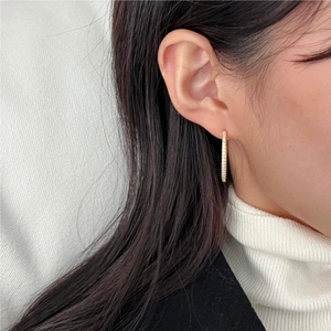Close-up of elegant gold slender earrings with pavé zircons on a female model