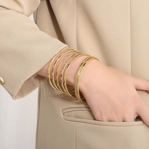 Dettaglio di sette bracciali impilati in acciaio al titanio dorato con finitura diamantata