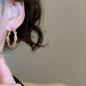 Detail of a golden twisted rope hoop earring on model showing metallic texture
