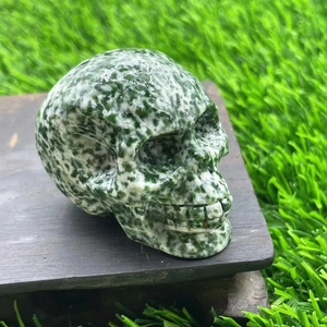 Detailed close-up of a 5cm carved gemstone skull with natural green and white spots