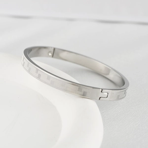 Detail of silver titanium steel bracelet featuring geometric Greek fret patterns and side clasp