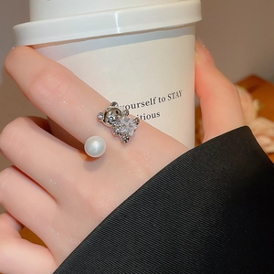 Detail of an open ring with a crystal-studded bear and a white pearl on the hand