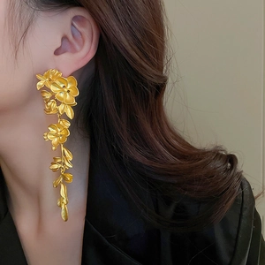 Close-up of model wearing gold floral tassel earrings with 3D petals and metallic luster