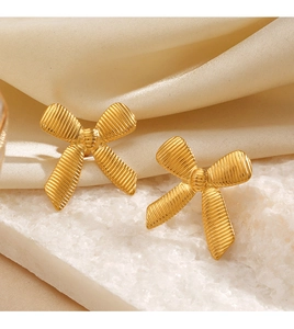 Macro shot of 18K gold-plated bow earrings with ribbed texture on silk background