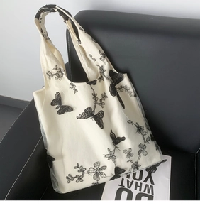 Close-up of butterfly embroidery and lace mesh detail on a beige canvas tote bag