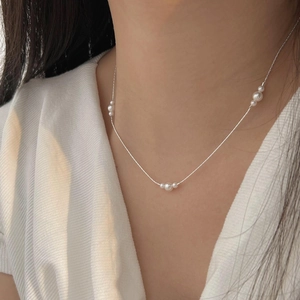 Close-up of a minimalist sterling silver necklace with delicate white pearls on a model