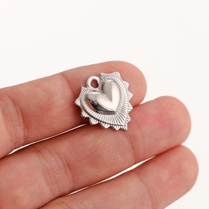 Close-up of a silver textured heart pendant held by fingers to show scale and detail