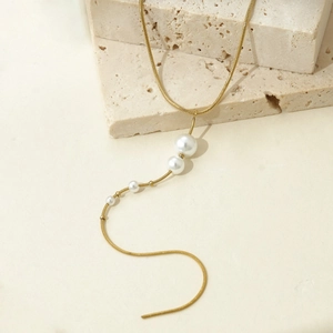 Elegant gold snake chain necklace with gradient white pearls on natural stone background
