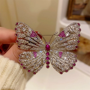 Detailed macro of hollow butterfly brooch featuring pink gemstones and pave crystals