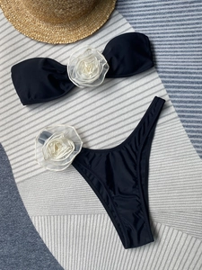 Flat lay of black bikini with oversized 3D white organza flowers on beach mat background