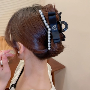 Detail of a large black hair claw clip with pearls and a satin bow on a hair bun