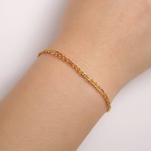 Close-up of a gold-plated stainless steel Figaro chain bracelet on a model wrist