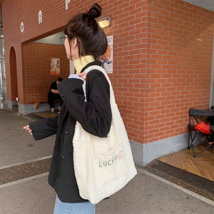 Close-up of white plush tote bag with green Lucky embroidery and orange smiley face