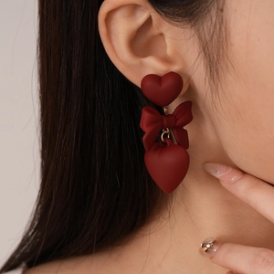 Close-up of vintage dark red bow and heart drop earrings on model with matte finish
