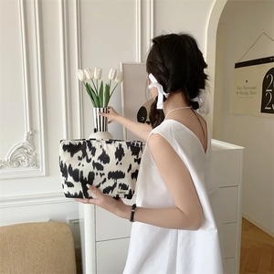 Close-up of a portable cow print makeup bag with zipper held by a model in a white dress