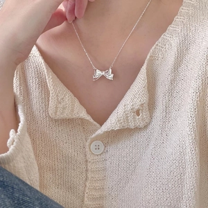 Close-up of minimalist S925 silver bow necklace worn on a cream knitted sweater
