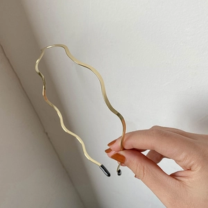 Detailed view of wave-shaped golden metal headband with black protective tips for women