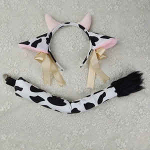 Detail view of plush cow ear headband and matching tail with black and white spots and bows