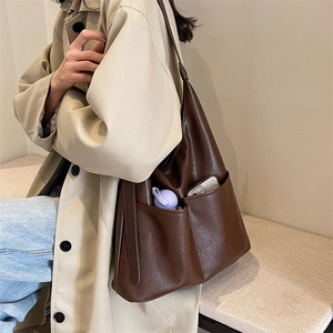 Detail view of large dark brown tote bag with two front pockets on soft leather surface