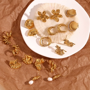 Detail of 18K gold plated stainless steel floral and geometric earrings on textured surface