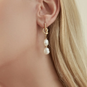 Baroque pearl drop earrings with golden knot design worn by a model in a close-up view