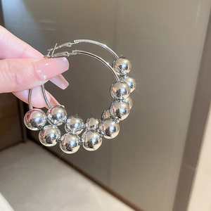 Gros plan sur les boucles d'oreilles créoles à perles argentées et sphères métalliques